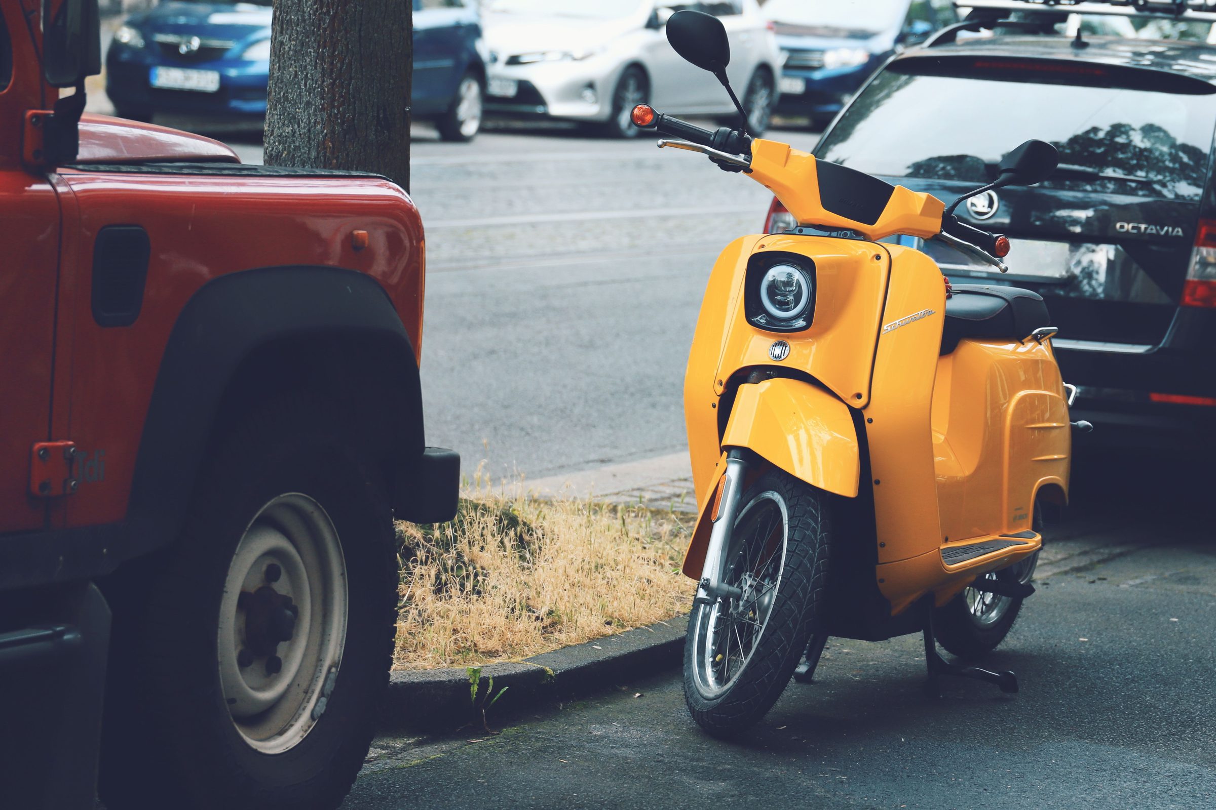 Yellow scooter parked on a city street next to a red ute