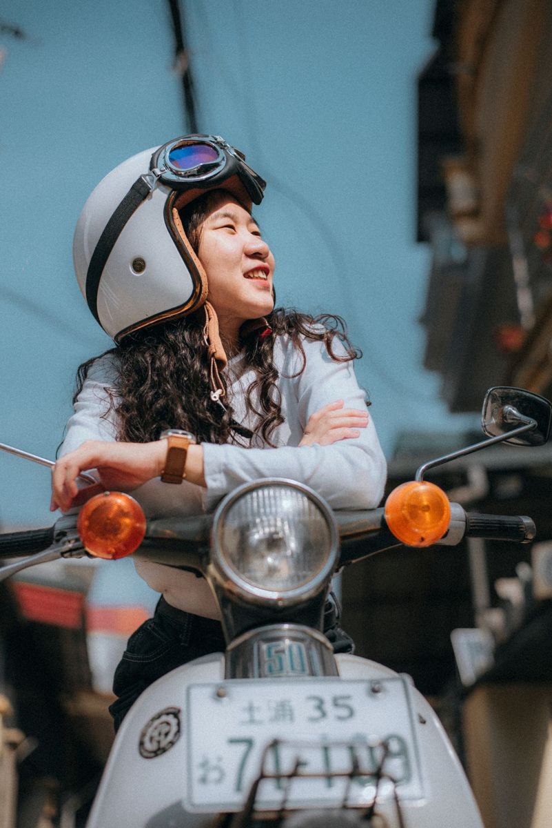 Smiling woman in a white helmet with goggles leaning on the handlebars of a white scooter